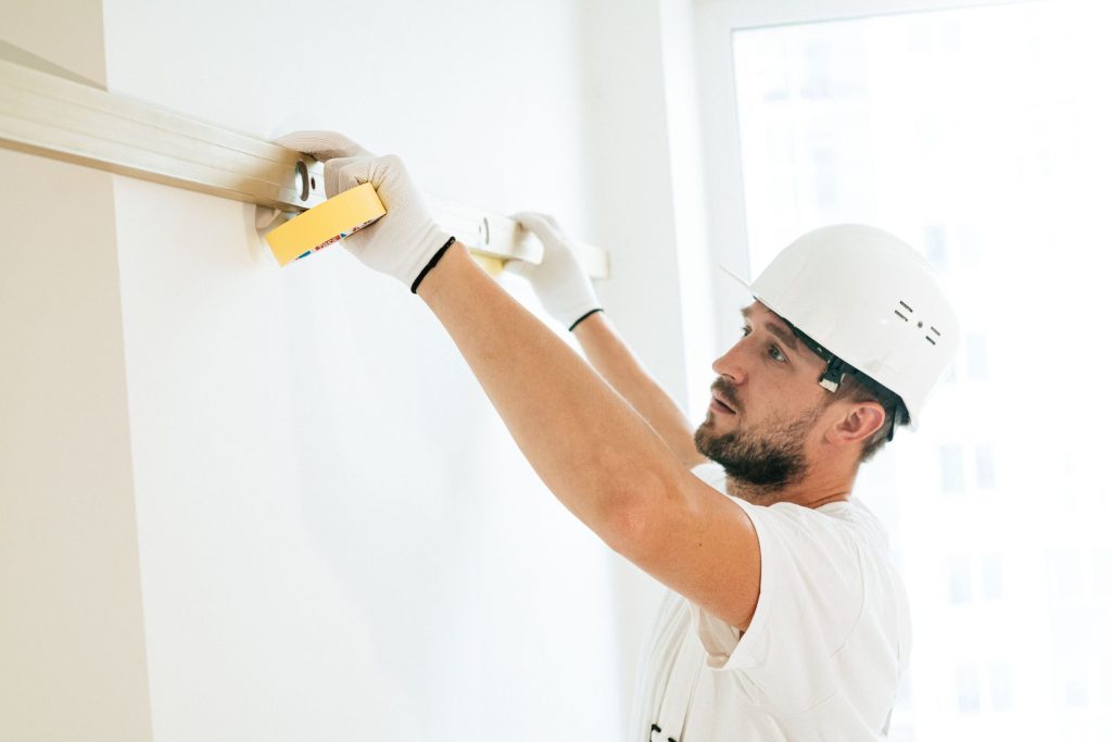 Ein Bauarbeiter misst im Innenbereich eine Wand mit einer Wasserwaage.