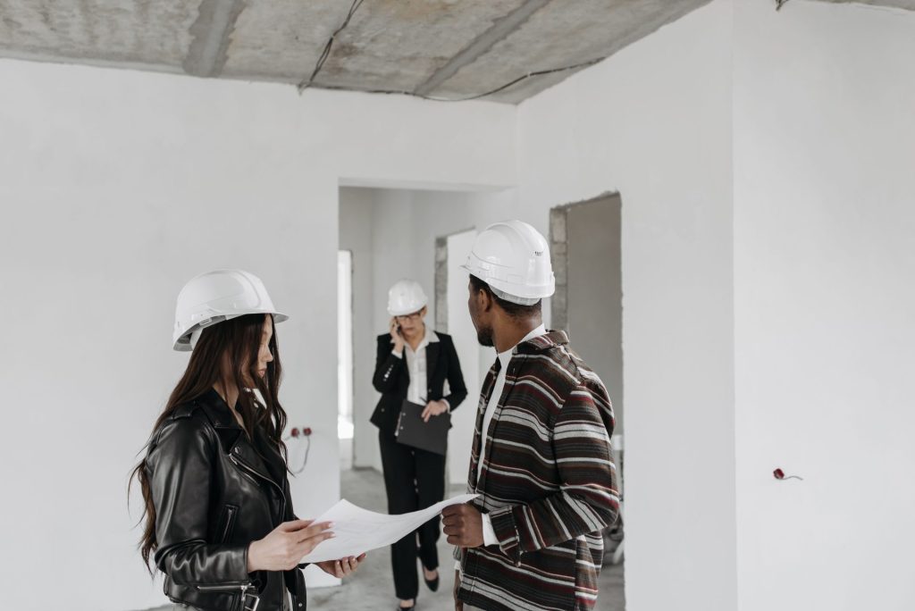 Ein diverses Bauteam mit Schutzhelmen begutachtet Baupläne auf einer Baustelle.